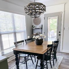 a dining room table with chairs and a vase on top of it in front of a window