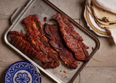 there are several pieces of meat in the pan on the floor next to some tortillas