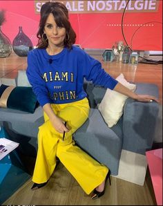 a woman sitting on top of a blue couch in front of a tv screen with her legs crossed