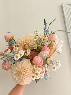 a hand holding a bouquet of flowers in front of a white wall with a window behind it