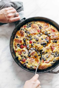 a person is cutting into a blueberry bread and butter pudding in a cast iron skillet