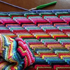 a crocheted blanket is sitting on a table next to a green knitting needle