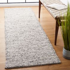 a large white rug on top of a wooden floor next to a plant in a vase