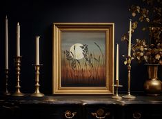 a painting and some candles on a shelf in front of a black wall with a gold frame