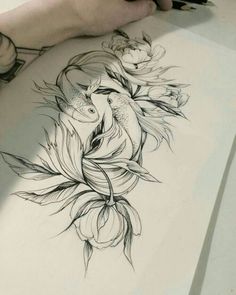 a drawing of a fish and flowers on a sheet of paper next to a person's hand