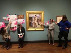 three women standing in front of a painting with sticky notes attached to it's walls