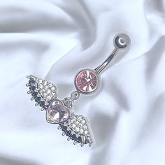 a pink belly button with an angel wing and heart shaped jewel in the center on a white satin background