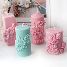 four pink and blue candles with flowers on them next to a framed photo in the background