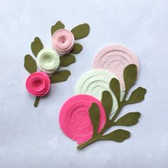 three felt flowers with green leaves and pink petals on white background, one is made out of paper