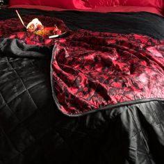 a black and red comforter on top of a bed next to a tray of food