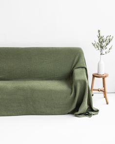 a green couch sitting next to a white vase on top of a wooden table in front of a white wall