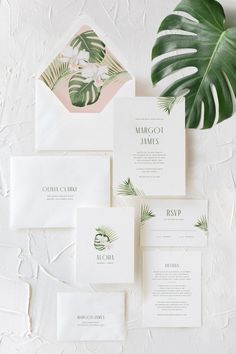 the wedding stationery is laid out on top of each other with tropical leaves and greenery