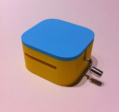 a small blue and yellow box with a key on the side sitting on a pink surface