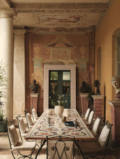 a dining room table and chairs in front of an ornate wall with paintings on it