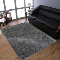 a living room with a black leather couch and wooden flooring next to a large window