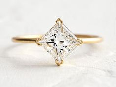 a yellow gold engagement ring with a princess cut diamond in the center, on a white background