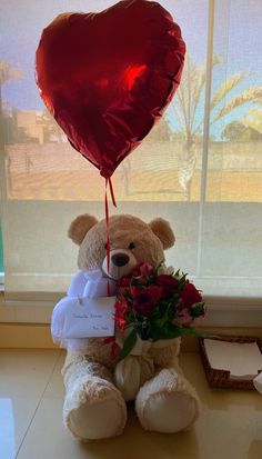 a teddy bear holding a heart shaped balloon with flowers and a tag attached to it