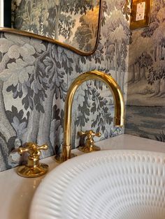 a bathroom sink with gold faucets and wallpaper