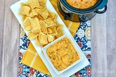 two plates with chips and dip next to a crock pot on a tablecloth