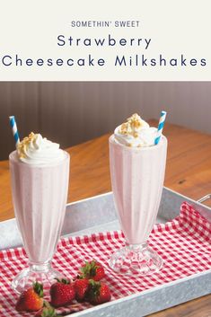 two strawberry milkshakes on a tray with strawberries