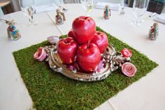 an arrangement of apples on a platter sitting on top of a green tablecloth