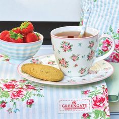 a cup of tea and some strawberries on a floral table cloth with a plate