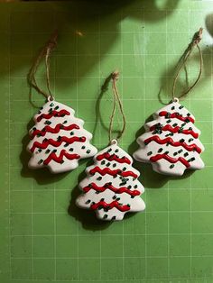 three decorated cookies hanging from twine on a green cutting board with white and red icing