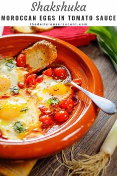 an orange bowl filled with eggs and tomatoes on top of a table next to bread