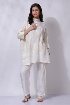 White aari hand embroidered pocho style tunic. Paired with a matching pant.
Components: 2
Pattern: Embroidered
Type Of Work: Aari
Neckline: High collar
Sleeve Type: Three-quarter
Fabric: 50% Silk, 50% Cotton
Color: White
Other Details: 
Attached cotton lining
Closure: Hook and Eye
Occasion: Resort - Aza Fashions Designer Wear Straight Kurta Tunic With Chikankari Embroidery, Designer Chikankari Embroidered Straight Kurta Tunic, Straight Kurta Tunic With Chikankari Embroidery, Designer Long Sleeve Pant Set With Resham Embroidery, White Naqshi Kurta For Spring, Embroidered Tunic Sets For Eid, Festive Long Sleeve Pant Set With Chikankari Embroidery, Embroidered Long Sleeve Pant Set For Designer Wear, Designer Chikankari Embroidery Tunic