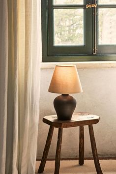 a lamp sitting on top of a wooden table next to a window with white curtains