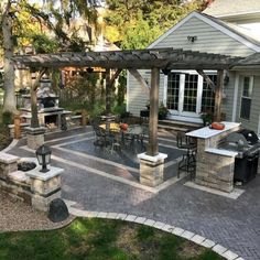 an outdoor kitchen and grill area in a backyard with brick pavers, stone patio furniture and pergolated decking