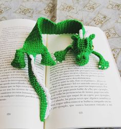 a crocheted bookmark shaped like a green dragon laying on top of an open book