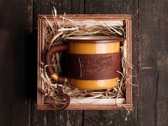 a coffee cup in a wooden box with straw on the bottom and brown leather wrapped around it