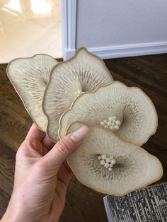 a hand holding three pieces of glass with white flowers on the bottom and one flower in the middle