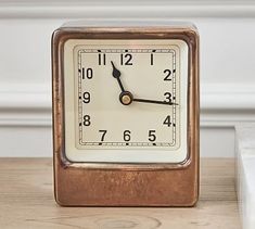 a small square clock sitting on top of a wooden table next to a white wall