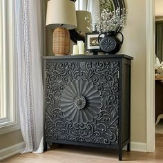 an ornate black cabinet with a mirror and vases on top of it in front of a window