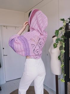 a woman in white pants and a pink crochet sweater is standing near a mannequin