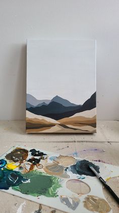 an easel with some paint on it next to a piece of art that looks like mountains