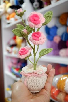 a crocheted planter with pink flowers is held in front of a shelf