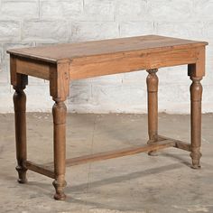 an old wooden table sitting in front of a white brick wall