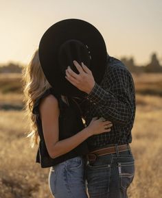 a man and woman kissing in the middle of a field with a cowboy hat on their head