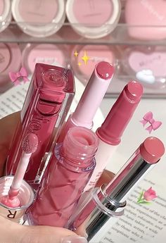 a person holding several pink lipsticks in their hand and some are on the table