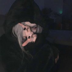 a woman with white hair and black makeup is wearing a hooded jacket while talking on the phone