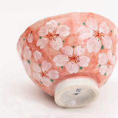 a pink vase with flowers painted on it's side, sitting on a white surface