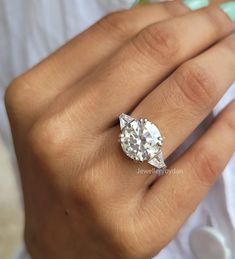 a woman's hand with a diamond ring on top of her finger and the other hand holding an engagement ring