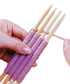 two hands are holding wooden sticks with purple beads on them and one hand is holding something