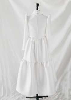 a white dress on a mannequin stand with a white background in the back