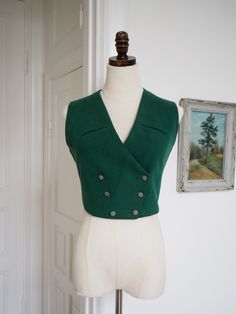 Dark green wool 1940s waistcoat with breast pockets. Double breasted and closes with dressed buttons. Such a stunner that will take any outfit to the next (very dapper!) level. Measurements: Bust 86 cm/ 33.8" Waist 70 cm/ 27.5" Length (at middle back) 40 cm/ 15.7" Excellent condition. Shows some wear to the neck of lining. Fitted Green Vest With Button Closure, Vintage Formal Winter Vest, Vintage Wool Vest For Formal Occasions, Green Buttoned Vest For Workwear, Retro Fitted Sleeveless Outerwear, Tailored Vintage Wool Vest, Vintage Fitted Sleeveless Outerwear, Fitted Sleeveless Vintage Outerwear, Vintage Buttoned Vest For Workwear