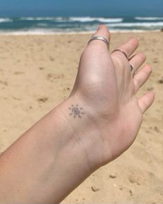 a person's hand with a small tattoo on it, in front of the ocean