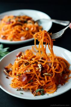 someone is eating spaghetti with carrots and bacon on the side, while holding a fork in their hand